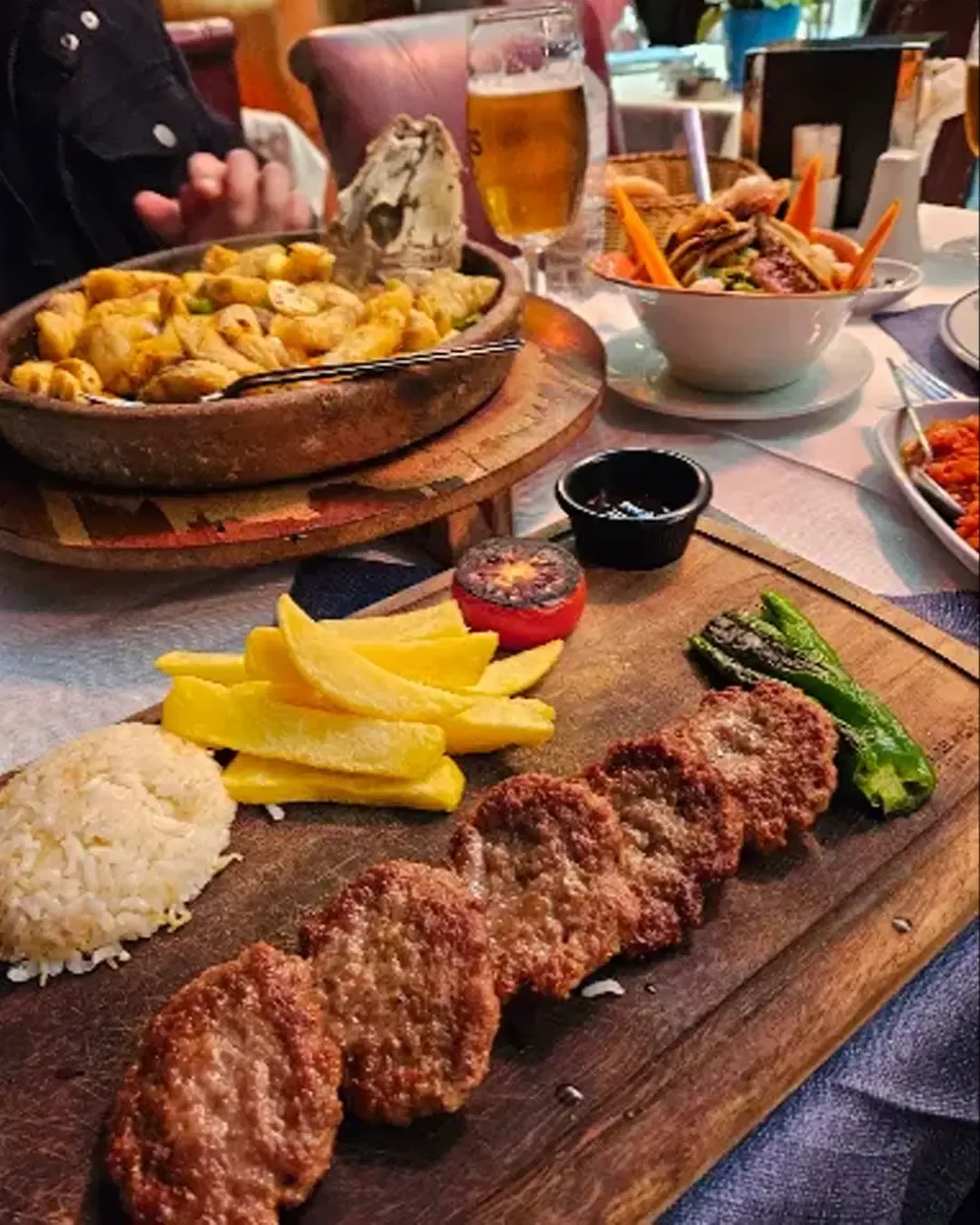 木の板にのったキョフテ(トルコ風ハンバーグ)、ライス、フライドポテト、焼きトマトとピーマン添え