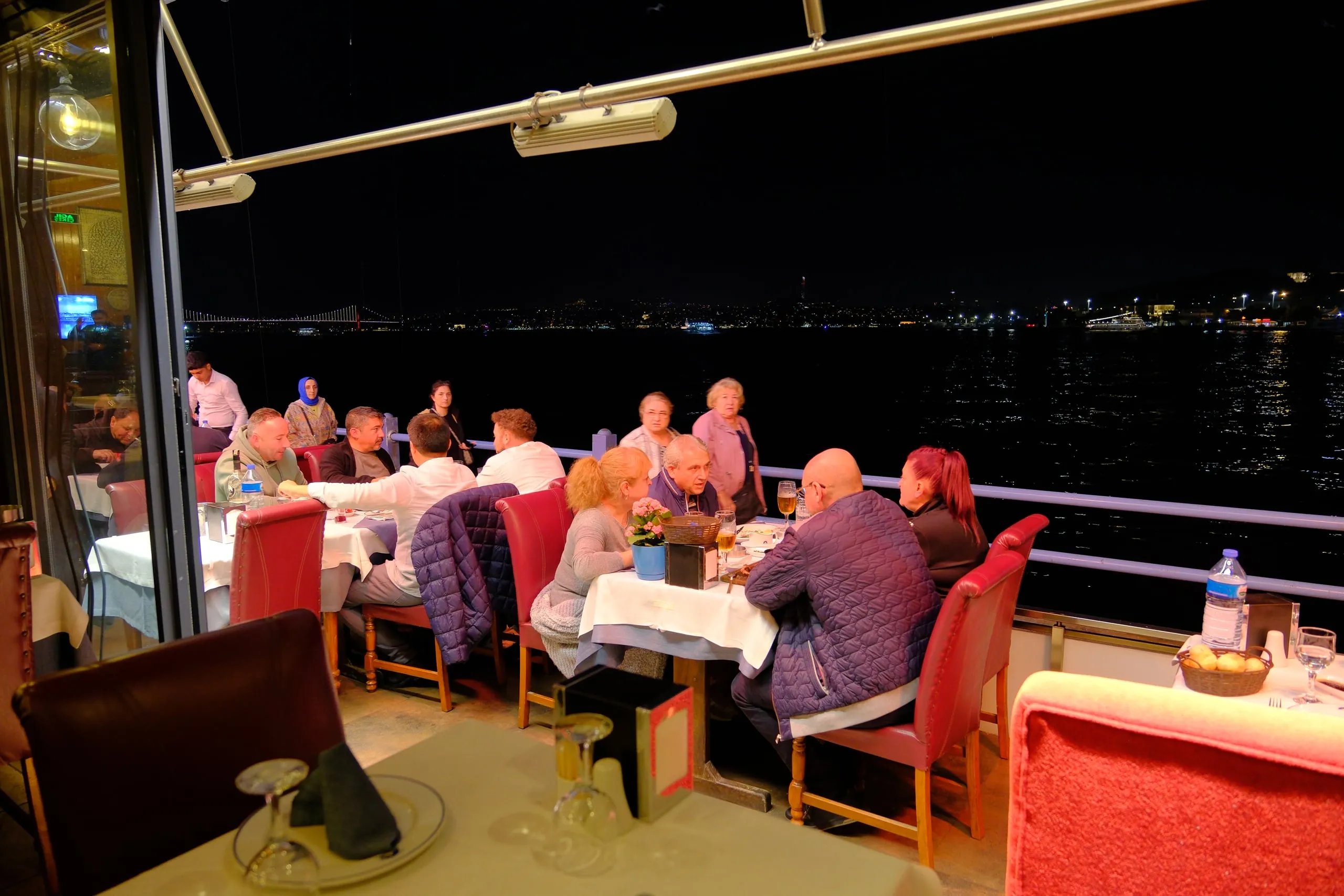 Open-air tables by the water at night next to the Galata Bridge